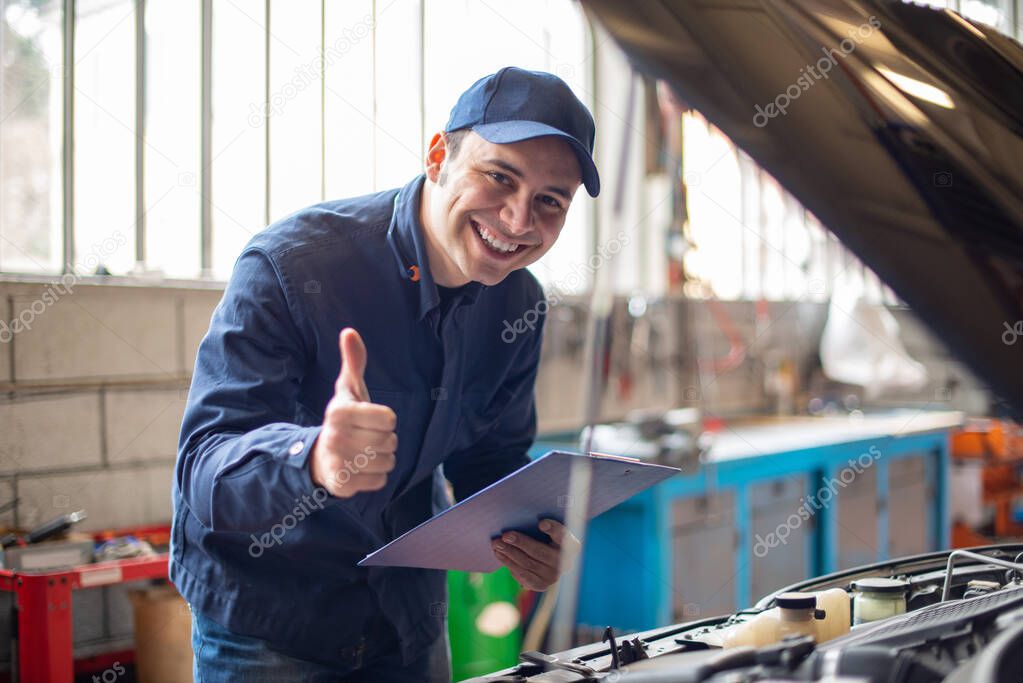 Smiling mechanic giving thumbs up in front of a car with the hood open