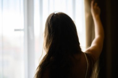 Mutlu kadın evde pencere perdelerini açıyor, arka manzara.