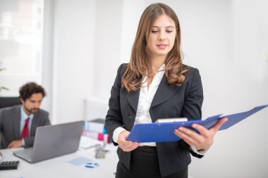 Genç gülümseyen iş kadını ofisinde bir belge okuyor.