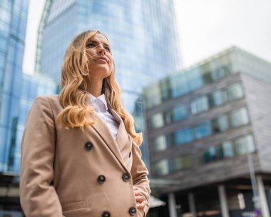 Şehir merkezinde duran gülümseyen sarışın bir kadının portresi.