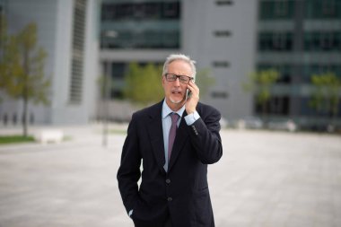 Şehir caddesinde yürürken cep telefonunu kullanan kıdemli bir işadamı.