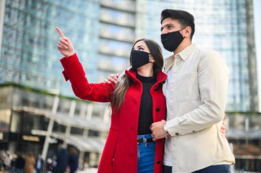 Covid ya da Coronavirus maskeli mutlu turistler bir şehirde birlikte yürürken ilginç bir nokta görüyorlar.