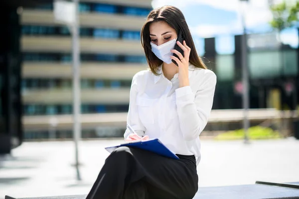 笑顔のビジネスマンの女性は 携帯電話で屋外に文書を書き Covid 19コロナウイルスパンデミックに対する保護マスクを着用しながら — ストック写真