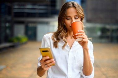 Güzel genç bayan yönetici dışarıda kahve içerken akıllı telefonunu kullanıyor.