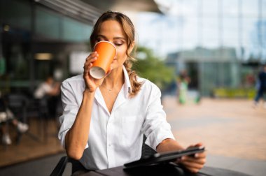 Genç iş kadını tabletini açık havada içerken kahve içiyor.