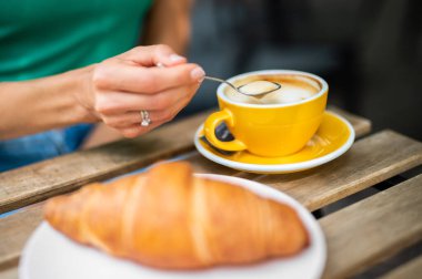 Kapuçino ve kruvasanla kahvaltı yapan bir kadının yakın çekimi.