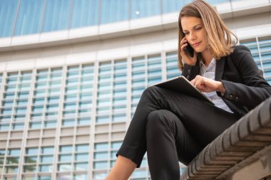 Elinde tabletle cep telefonunu kullanan gülümseyen genç bir iş kadını.