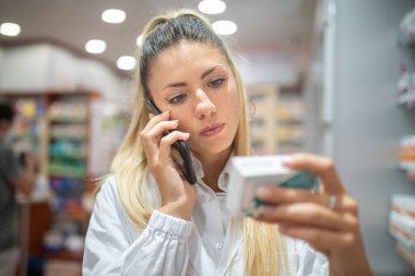 Eczacı telefonda konuşurken eczanede ilaç kontrolü yapıyor.