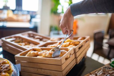 Otel kahvaltısı, büfeden çörek alan adam.