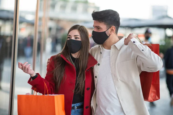 コヴィドとコロナウイルスのショッピング街を歩きながら買い物袋を持っている若いカップル — ストック写真