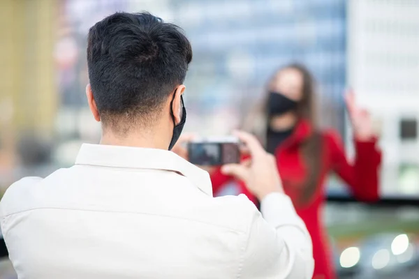 男の写真を撮る彼のガールフレンド屋外ながら身に着けている保護マスクに対してCovid Coronavirusパンデミック — ストック写真