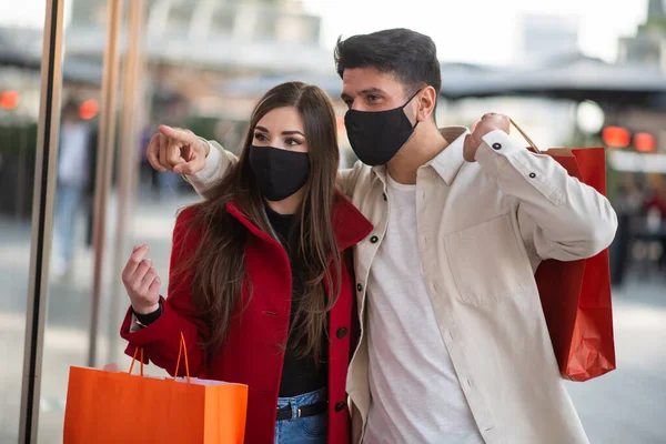 コヴィドとコロナウイルスのショッピング街を歩きながら買い物袋を持っている若いカップル — ストック写真