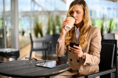 Kahve molasında olan genç iş kadını akıllı telefonunu kullanıyor.