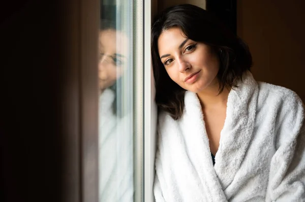 バスローブを着てホテルの部屋の窓の上に寝そべっていた若い女性 — ストック写真