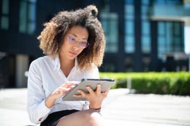Afro-Amerikalı iş kadını iş ortamında dijital tabletini açık havada kullanıyor.