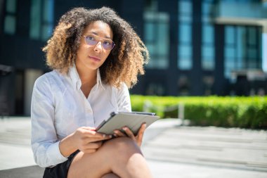 Afro-Amerikalı iş kadını iş ortamında dijital tabletini açık havada kullanıyor.