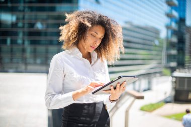 Afro-Amerikalı iş kadını iş ortamında dijital tabletini açık havada kullanıyor.