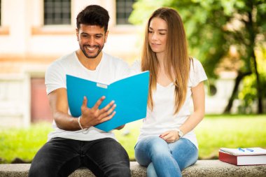 İki öğrenci açık hava bankında birlikte ders çalışıyor.