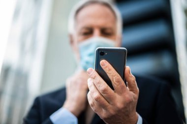 Üst düzey yönetici Coronavirus salgınından korunmak için maske takarken akıllı telefonunu açık havada kullanır.