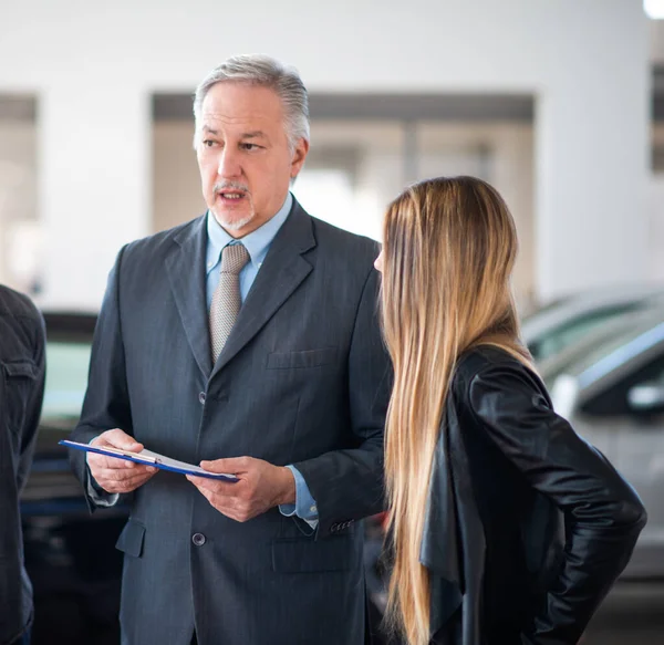 Young family talking to the salesman and choosing their new car in a showroom