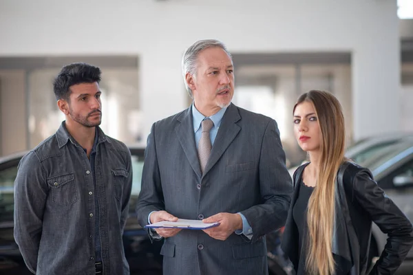 Jovem Família Conversando Com Vendedor Escolhendo Seu Novo Carro Showroom — Fotografia de Stock