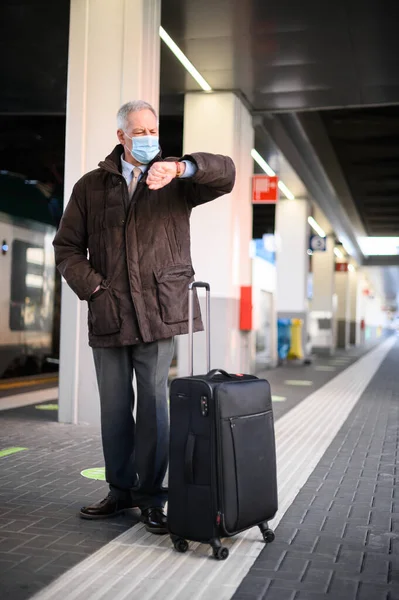 シニア男身に着けていますA保護マスクに対してCovid 19でA鉄道駅チェック時間 — ストック写真