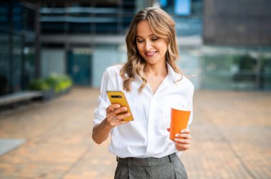 Güzel genç bayan yönetici dışarıda kahve içerken akıllı telefonunu kullanıyor.