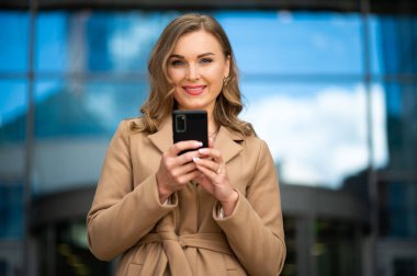 Güzel genç bayan yönetici dışarıda akıllı telefonunu kullanıyor.