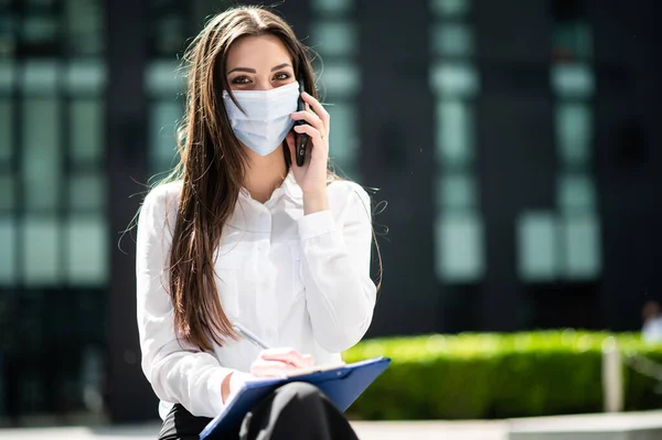 笑顔のビジネスマンの女性は 携帯電話で屋外に文書を書き Covid 19コロナウイルスパンデミックに対する保護マスクを着用しながら — ストック写真