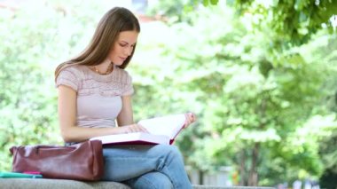 Güzel bir üniversite öğrencisi parkta bir bankta kitap okuyor.