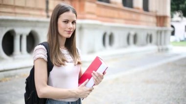 Okulunun önünde kitap tutan genç bir kız öğrenci, ağır çekimde.