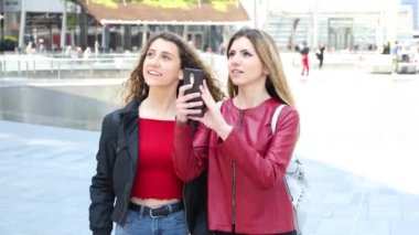 Modern bir şehirde yürürken fotoğraf çeken iki kadın arkadaş