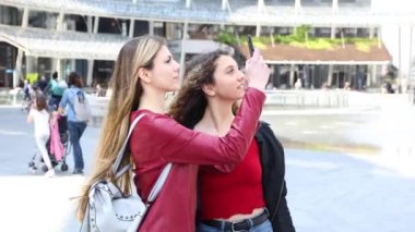 Modern bir şehirde yürürken fotoğraf çeken iki kadın arkadaş