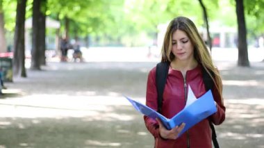 Gülümseyen öğrenci elinde kitapla geziyor.