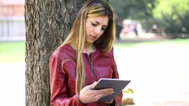 Mujer Joven Usando Una Tableta Digital Tumbada Contra Árbol Parque — Vídeo de stock