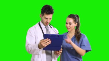 İki genç doktor yeşil ekran krom anahtar arka planında izole edilmiş bir panoda bir kağıda bakıyor.