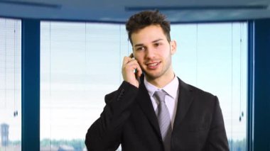 Gülümseyen işadamı ofisinde telefonla konuşuyor.