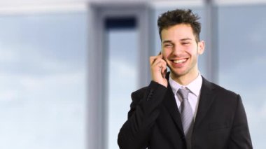 Gülümseyen işadamı ofisinde telefonla konuşuyor.