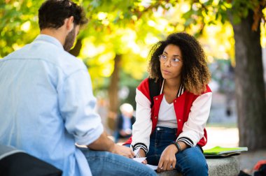 İki çok ırklı öğrenci açık bir bankta birlikte okuyorlar.