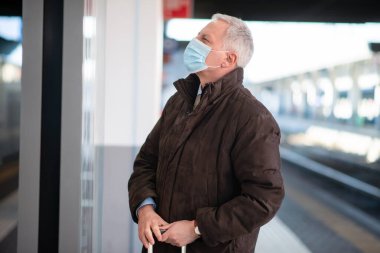 Maskeli kıdemli işadamı treni bekliyor, covid ve coronavirüs hareketlilik konsepti