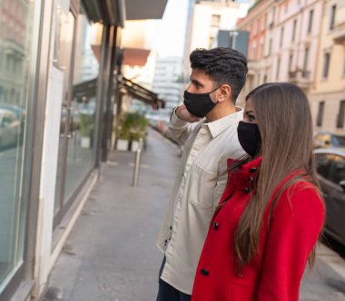 Covid ve Coronavirus alışveriş yapıyor, genç bir çift şehirde yürüyor.