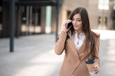 Şehir caddesinde kahve içerken telefonla konuşan genç bir iş kadını.