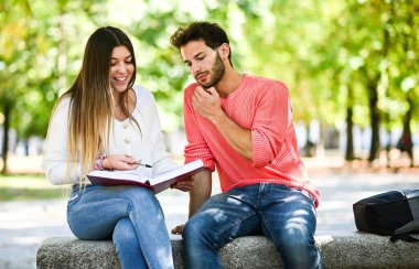 İki öğrenci açık hava bankında birlikte ders çalışıyor.