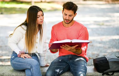 İki öğrenci açık hava bankında birlikte ders çalışıyor.
