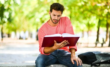 Yakışıklı genç adam parkta bankta kitap okuma