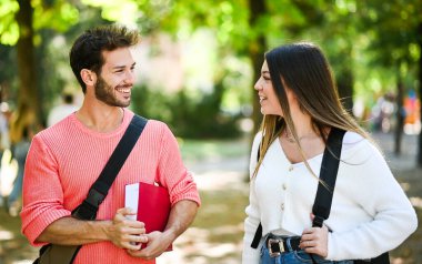 İki öğrenci, erkek ve kadın, bir üniversite parkında kitap tutarken dışarıda konuşuyorlar.