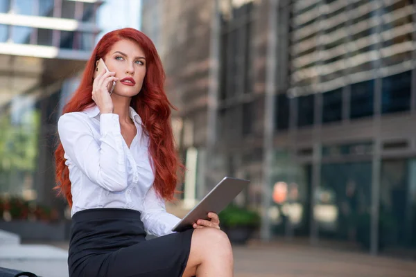 タブレットを屋外に持ちながら携帯電話を使っている若いビジネス女性 — ストック写真
