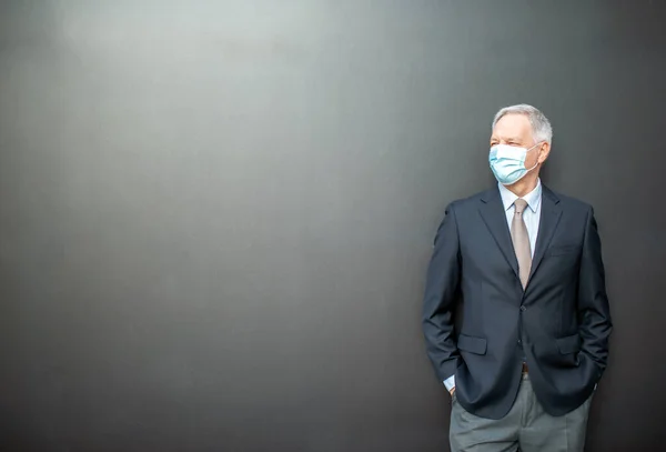 コロナウイルスCovidの概念黒壁の隣に立つ覆面のある高級ビジネスマン — ストック写真
