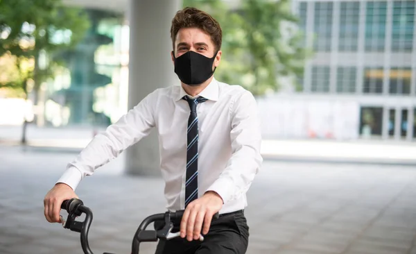 Masked businessman parking his bicycle in front of the office