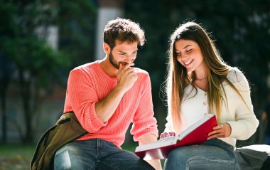 İki öğrenci açık hava bankında birlikte ders çalışıyor.